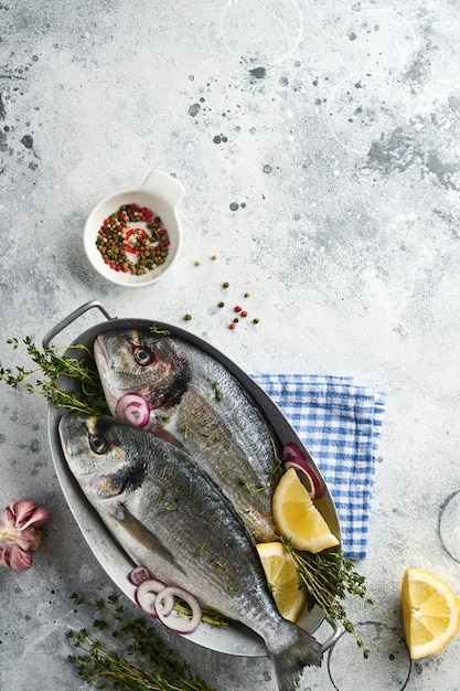 Peixe fresco dourado cru ou pargo com ingredientes para fazer limão, tomilho, alho, tomate cereja e sal sobre fundo de ardósia cinza claro, pedra ou concreto. Vista superior com espaço de cópia.