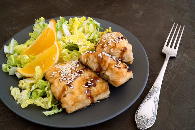 Peixe frito com salada num prato cinza.