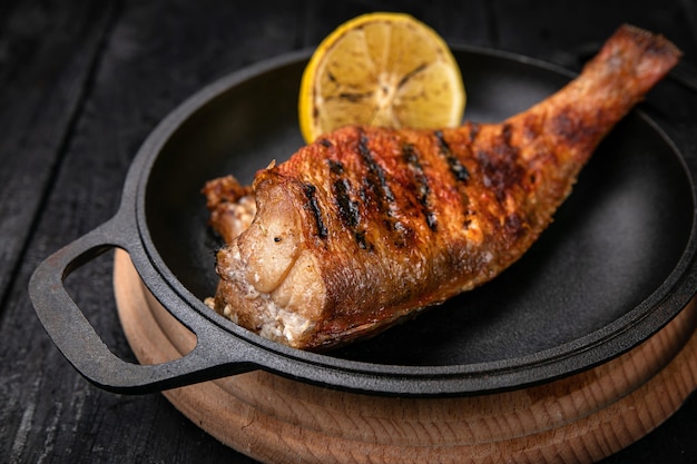 Peixe frito em uma panela preta sobre uma mesa de madeira escura