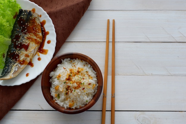 Peixe frito na chapa branca, pauzinho, guardanapo, arroz na parte superior de madeira para o espaço