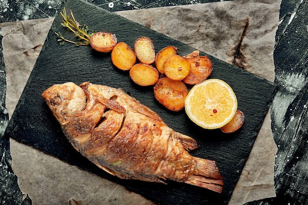 Peixe inteiro grelhado servido com batatas assadas, limão e molho. vista do topo.