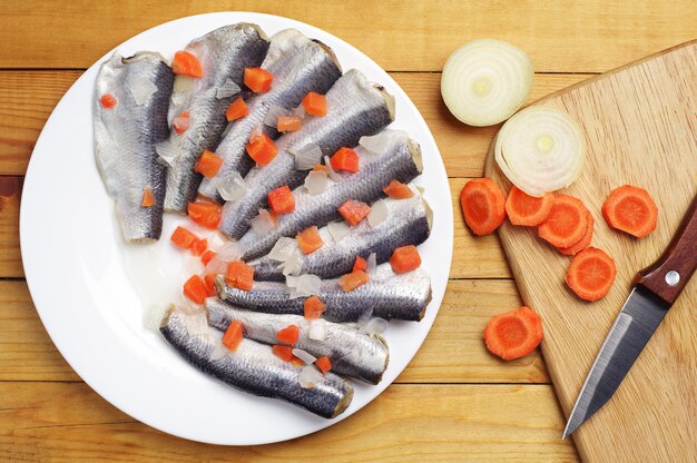 Peixe marinado com cenoura em um prato na mesa de madeira. Vista do topo