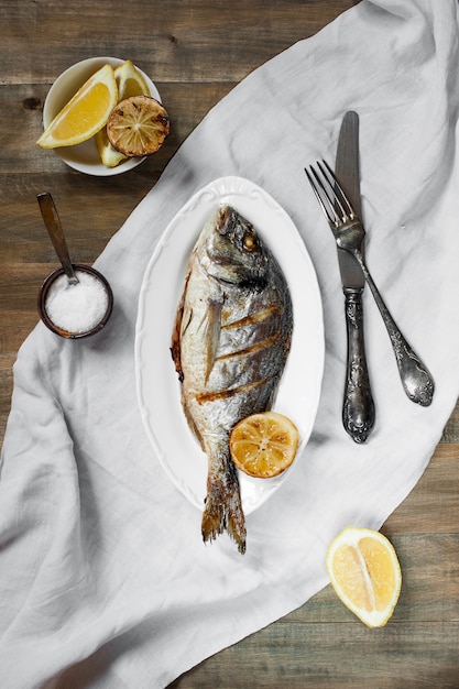 Peixe preparado no prato branco, na mesa de madeira velha