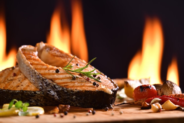 Peixe salmão grelhado e vários legumes na mesa de madeira