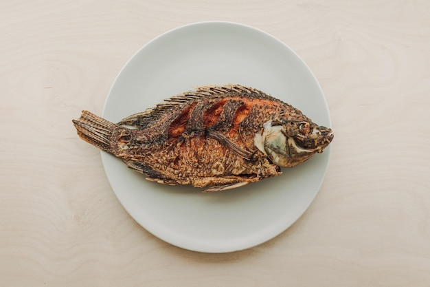 Peixe tailandês cozido servido em mesa de madeira branca