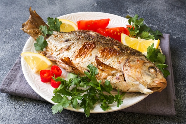 Peixes cozidos da carpa com vegetais e especiarias em uma placa em uma tabela escura com uma cópia do espaço.