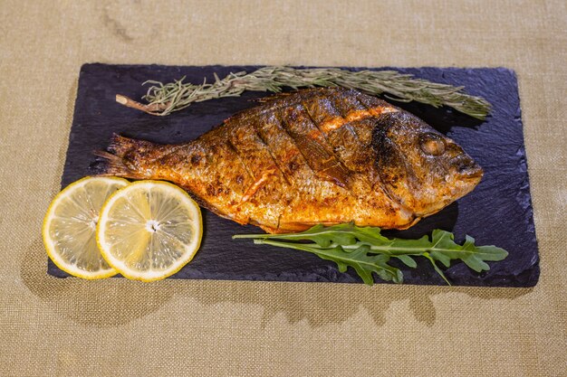 Peixes de gilthead assados com limão, ervas, sal em fundo preto. Conceito de comida saudável. Quadro de comida.