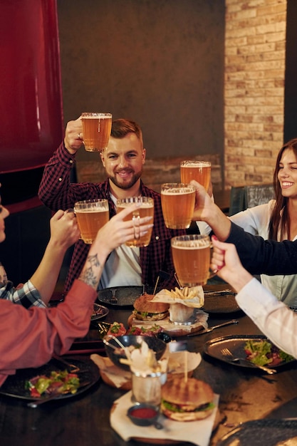 Pela mesa Grupo de jovens amigos sentados juntos no bar com cerveja