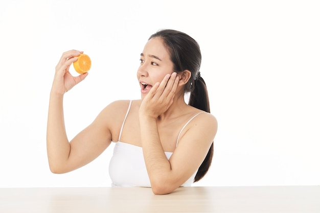 Pele perfeita e fresca. Retrato de mulher jovem e bonita sorridente com laranja em fatias, isolada na superfície branca. Conceito de mulher saudável