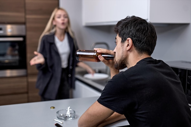 Pelea familiar. Familia caucásica joven infeliz durante el conflicto en la cocina en casa. Concéntrese en el consumo masculino de cerveza alcohólica. Pareja casada discutiendo, el hombre ignora, mirando a un lado.