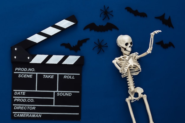 Película de terror, tema de halloween. Claqueta de cine, esqueleto, arañas y murciélagos decorativos voladores en el clásico azul oscuro
