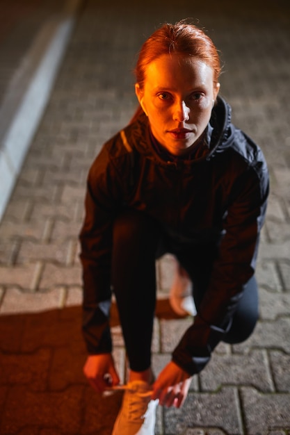 Pelirroja atleta femenina atar cordones en el corredor de la calle atar zapatos para correr mientras se ejecuta en la ciudad de noche ...