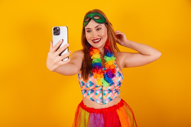 Pelirroja brasileña en ropa de carnaval con un collar de flores alrededor de su cuello mostrando smartphone