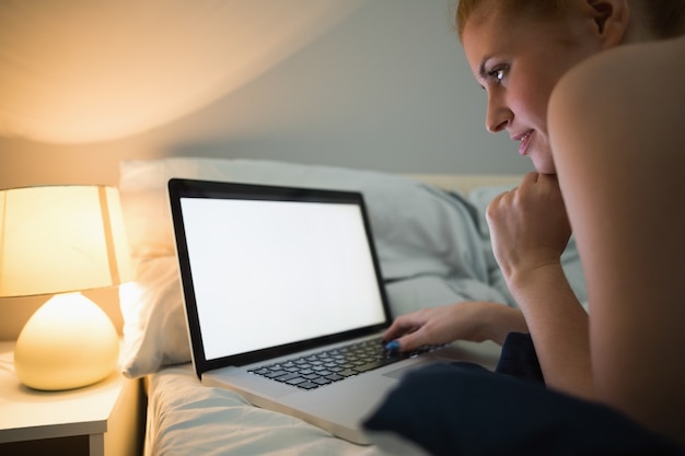 Pelirroja joven acostada en su cama usando la computadora portátil