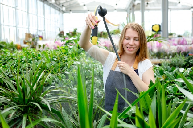 Pelirroja joven trabajadora en el mercado de plantas invernadero vertiendo plantas y sonriendo