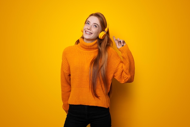 Pelirroja mujer caucásica aislada sobre fondo amarillo escuchando música con auriculares