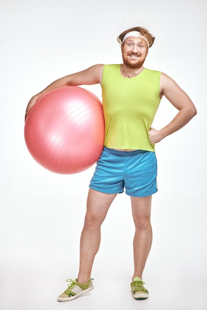 Pelirrojo barbudo hombre regordete está sosteniendo una pelota de fitness