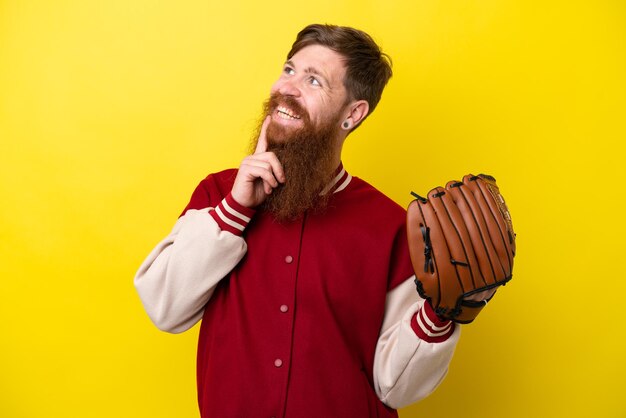 Pelirrojo jugador hombre con barba con guante de béisbol aislado sobre fondo amarillo mirando hacia arriba mientras sonríe