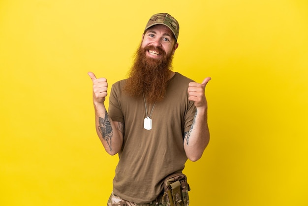 Pelirrojo militar con placa de identificación aislado sobre fondo amarillo con gesto de pulgar hacia arriba y sonriente