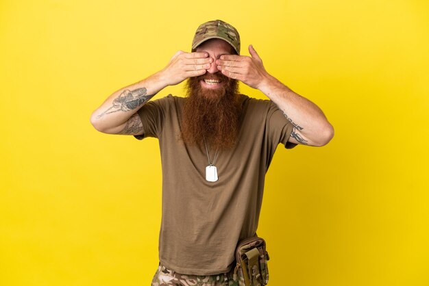Pelirrojo militar con placa de identificación aislado sobre fondo amarillo que cubre los ojos con las manos