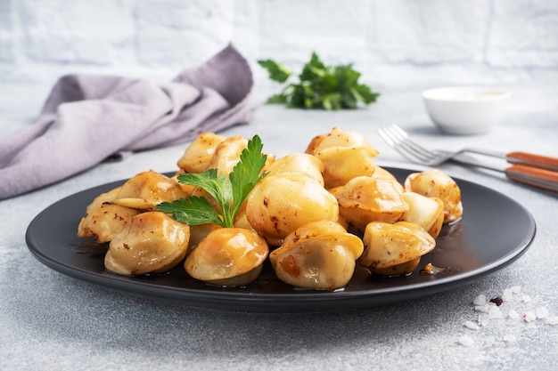 Pelmeni frito tradicional, ravióli, bolinhos de massa recheados com carne na placa preta, cozinha russa. Mesa de concreto cinza, copie o espaço.