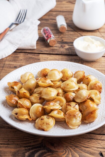 Pelmeni frito tradicional, ravióli, bolinhos recheados com carne no prato, cozinha russa. mesa de madeira rústica, copie o espaço.