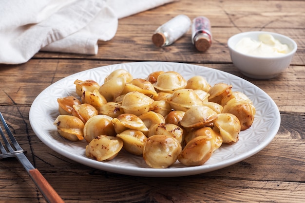 Pelmeni frito tradicional, ravióli, bolinhos recheados com carne no prato, cozinha russa. Mesa rústica de madeira, copie o espaço.