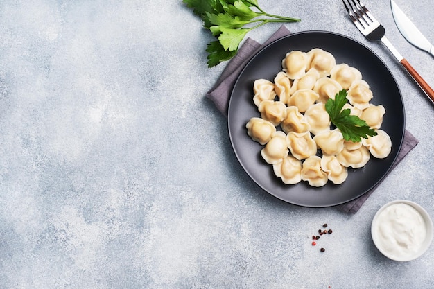 Pelmeni tradicional, ravioles, bolas de masa rellenas de carne en un plato, cocina rusa. Fondo de hormigón claro, copie el espacio.