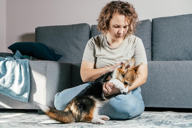 Pelo rizado alegre alegre mujer descalza con perro corgi Obediencia entrenamiento alimentación animal sentado y jugando