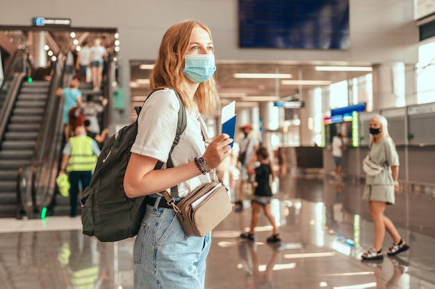 Pelo rubio mujer turista mano sosteniendo pasaporte con maleta equipaje área de espera de la terminal del aeropuerto para un viaje. Viajar después de la pandemia de Covid-19