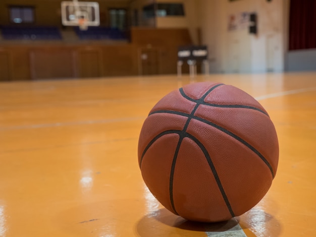 Pelota de baloncesto en la cancha con línea de tiros libres, canasta fuera de foco en el fondo.