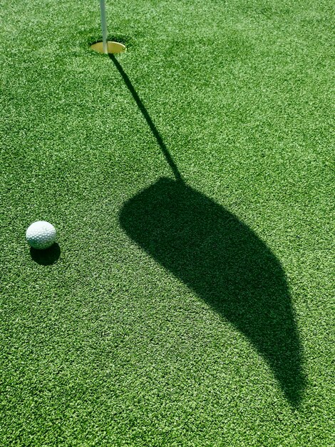 Pelota de golf en el green, la sombra de una bandera en un campo de golf verde