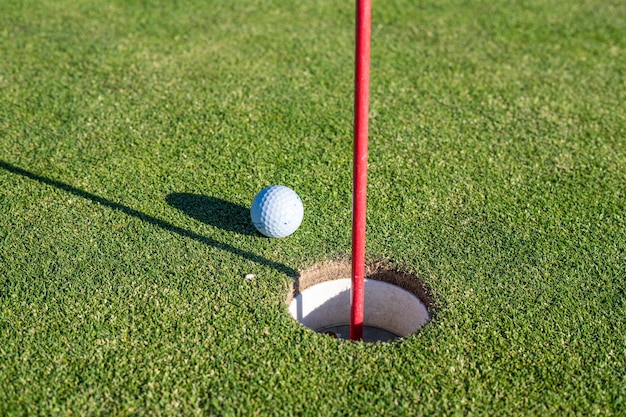 Una pelota de golf junto a un hoyo en un campo de golf