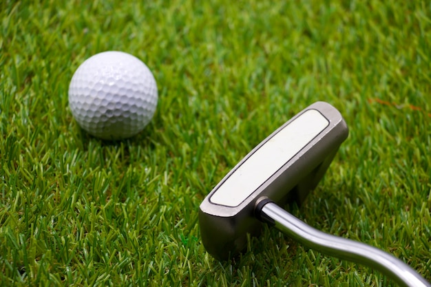 La pelota de golf y el putter están en hierba verde