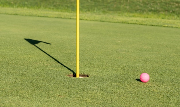 Pelota de golf rosa por bandera y agujero en green