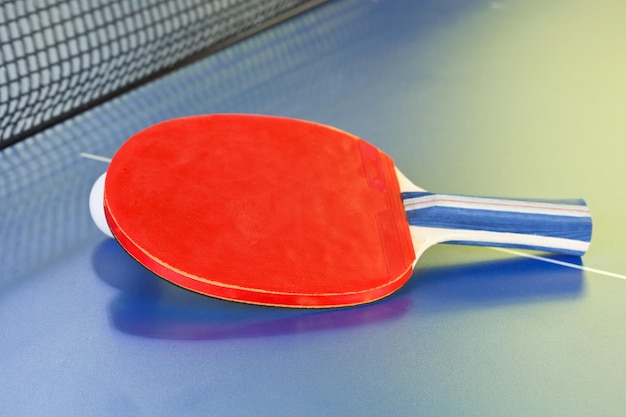 Pelota de tenis de murciélago rojo en mesa de ping pong azul