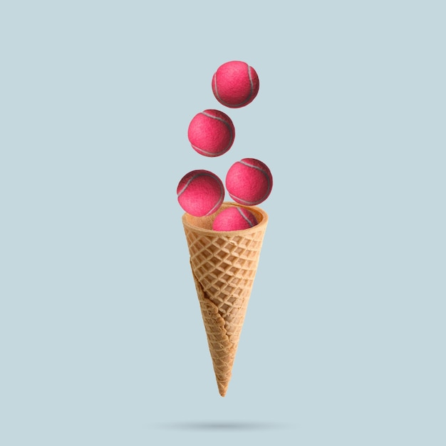 Una pelota de tenis rosa sale volando de un cono de helado sobre un fondo azul pastel. Concepto de tenis.