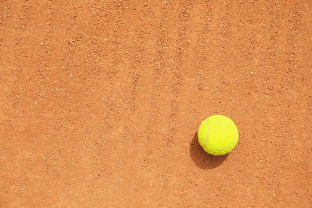 Pelota de tenis verde claro sobre tierra batida, espacio para texto