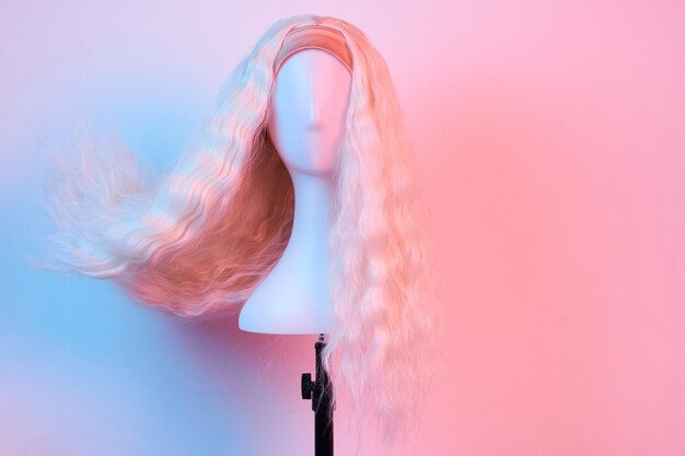 Peluca rubia de aspecto natural en la cabeza blanca del maniquí Cabello largo en el soporte de la peluca de plástico aislado en fondo blanco Iluminación rosa vista delantera