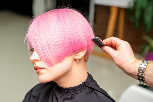 Una peluquera está peinando el pelo corto teñido de rosa de la clienta en una peluquería