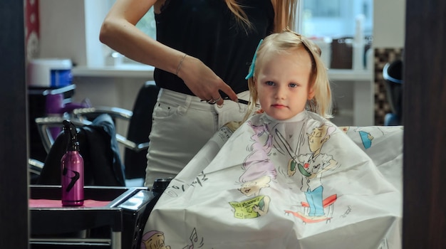 La peluquera hace un bonito peinado de moda para una linda niña rubia