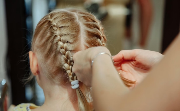 La peluquera hace un bonito peinado de moda para una linda niña rubia