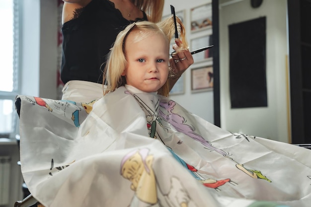 La peluquera hace un bonito peinado de moda para una linda niña rubia