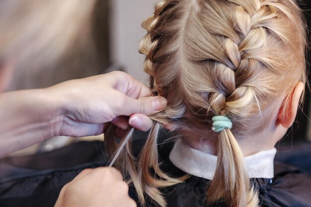 La peluquera hace un peinado bonito a la moda para una niña linda