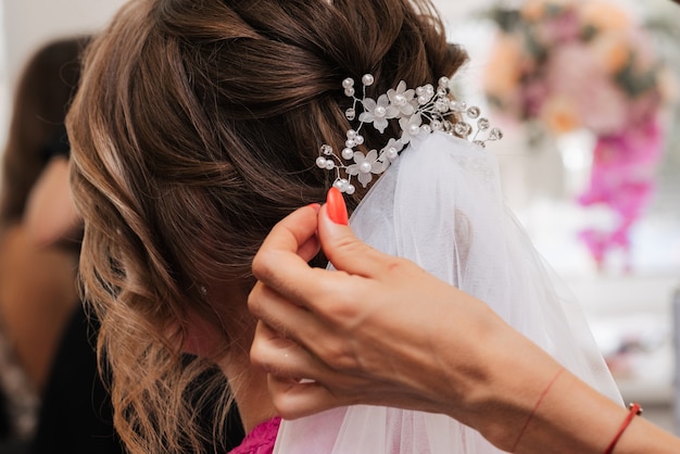 La peluquera hace un peinado elegante para el peinado de la novia con joyas blancas en su cabello en el salón.