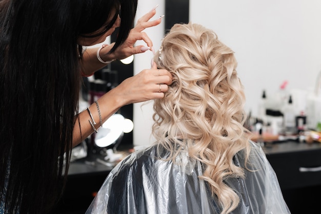 Una peluquera hace un peinado festivo para una rubia en un salón de belleza.