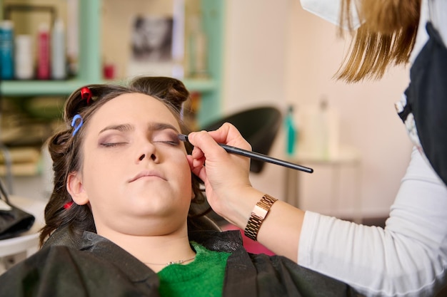 peluquera maquillando y peinando a una joven clienta en un salón de belleza