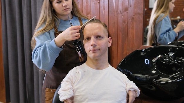 Una peluquera en un salón de belleza hace un corte de pelo y un peinado para un hombre con discapacidad