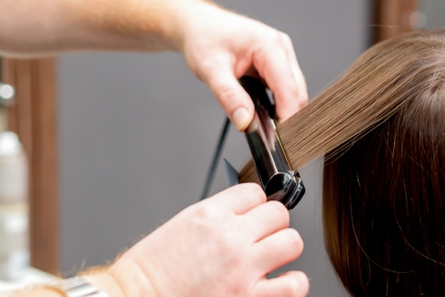 Peluquería alisa el cabello de la mujer.