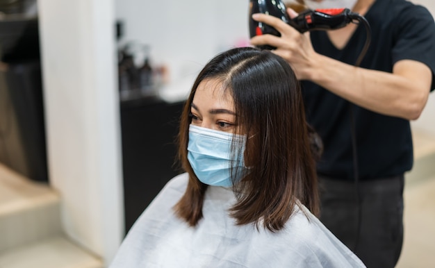 Peluquería cortando el cabello a una clienta usando una máscara médica para proteger el coronavirus